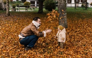 Man playing with a baby in a bed of leaves