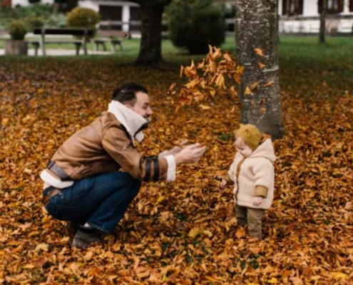 Man playing with a baby in a bed of leaves