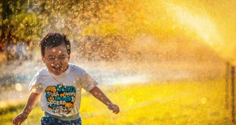 Child playing with water from sprinklers