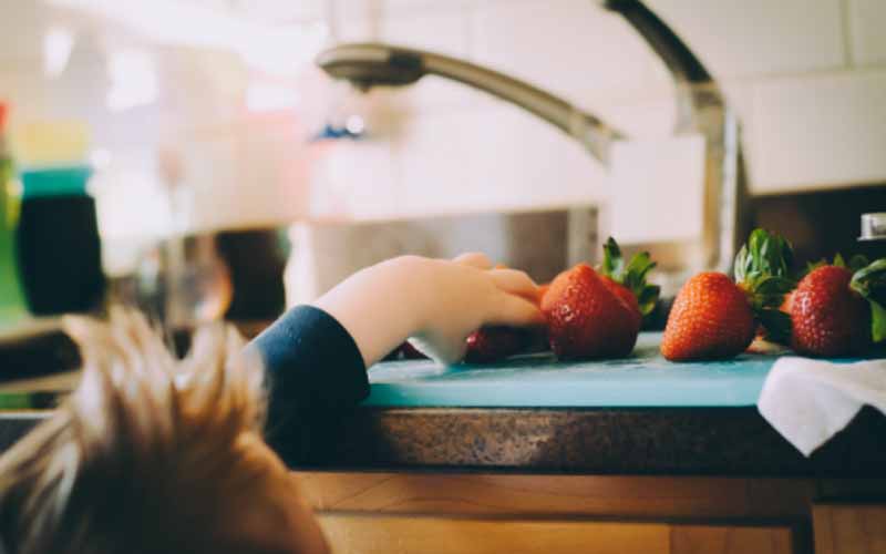 Child reaching for strawberries on the kitchen counter